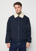 Marineblaue isolierte Jacke mit einem flauschigen cremefarbenen Kragen, Reißverschluss und Seitentaschen; zeichnet sich durch eine glatte, weiche Textur aus.