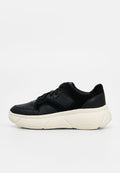 Schwarzer Schnürsneaker mit perforiertem Lederobermaterial und dicker weißer strukturierter Sohle, Seitenansicht auf hellem einfarbigem Hintergrund.