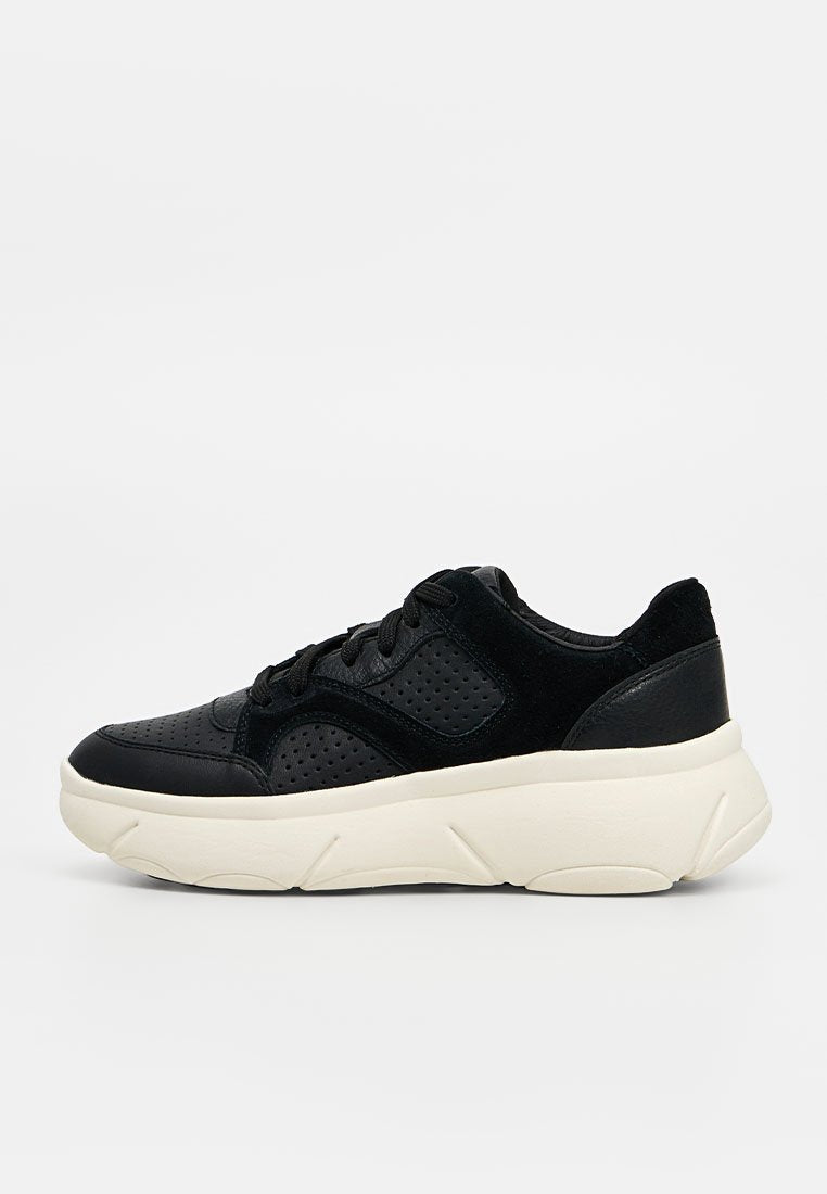 Schwarzer Schnürsneaker mit perforiertem Lederobermaterial und dicker weißer strukturierter Sohle, Seitenansicht auf hellem einfarbigem Hintergrund.