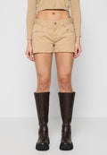 Beige Denim-Shorts mit ausgefranstem Saum, vorderen Taschen und metallischem Knopfverschluss, kombiniert mit hohen braunen Lederstiefeln mit Schnallen.