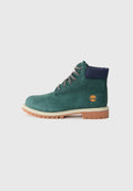 Grüne Wildleder-Stiefeletten mit einem marineblauen Kragen, grauen Schnürsenkeln und einer braunen Gummisohle mit einem Baum-Logo an der Seite.