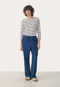 Blaue Jeans mit einem elastischen Bund und Kordelzug, kombiniert mit einem langärmeligen Oberteil in Weiß und Marineblau mit Streifen. Flache Sandalen.