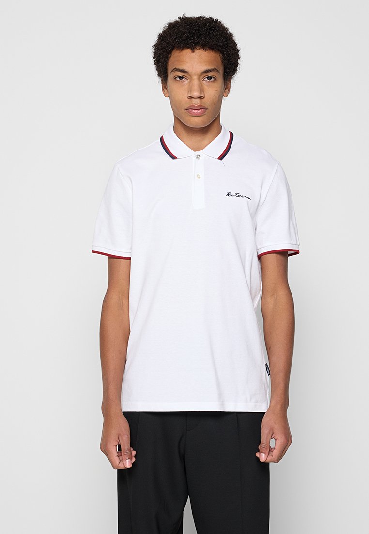 Weißes Poloshirt aus Baumwolle mit einer Zweiknopf-Leiste, einem rot-blauen gestreiften Kragen und einem gestickten Logo auf der Brust.