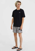 Schwarzes Baumwoll-T-Shirt, gemusterte graue Shorts mit schwarzem Logo und schwarze Flip-Flops. Modell steht vor einem schlichten weißen Hintergrund.