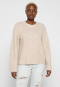 Beiger, flauschiger Pullover mit rundem Halsausschnitt, überschnittenen Schultern und langen Ärmeln. Kombiniert mit hellblauen Jeans mit Used-Look.
