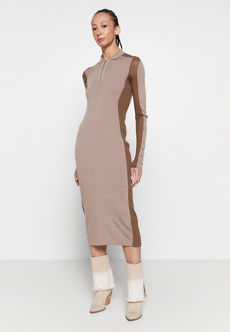 Rippstrick-Kleid mit langen Ärmeln in Beige, mit braunen Seitenpaneelen und einem Viertel-Reißverschlusskragen. Stylisch kombiniert mit cremefarbenen und beigen Stiefeletten.