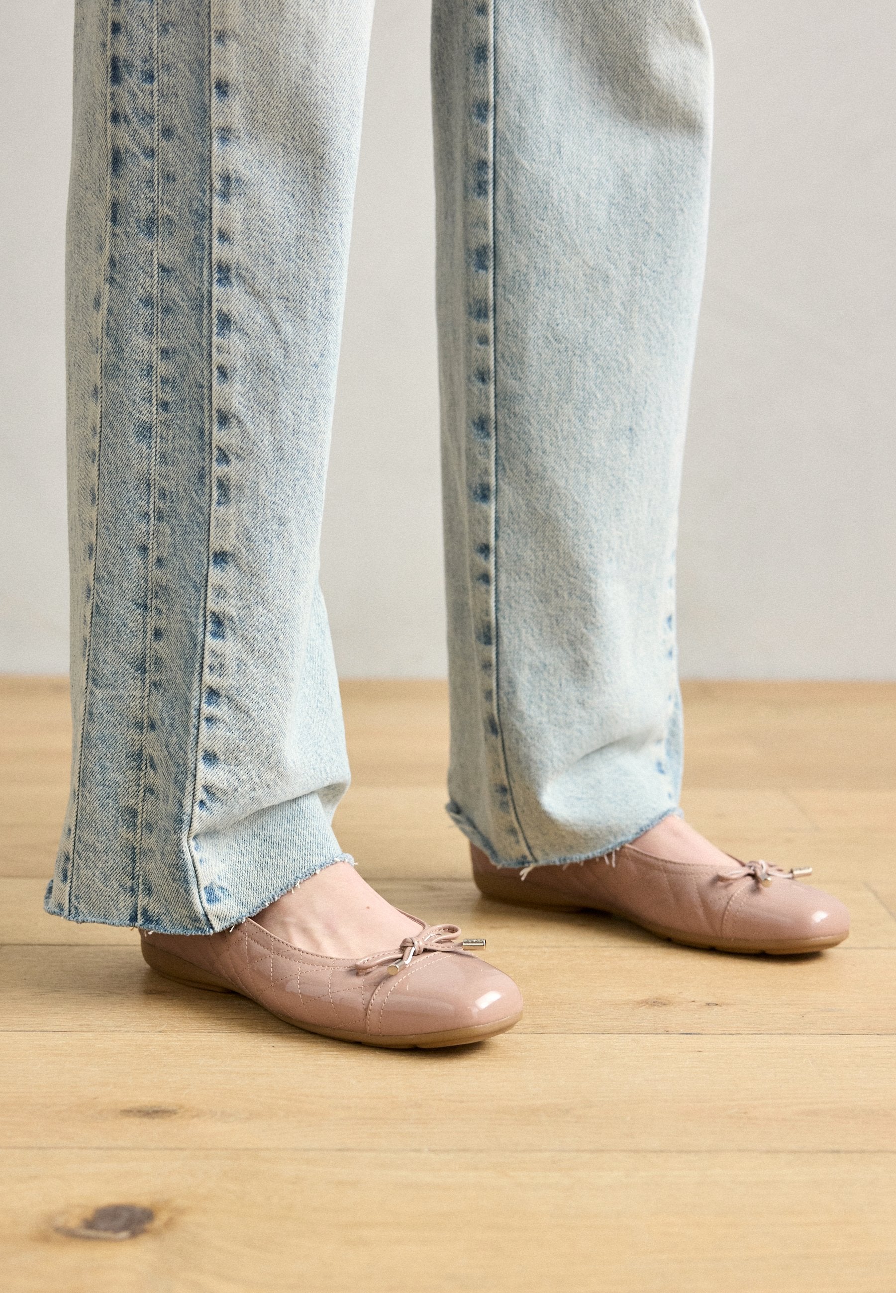 Helle rosa patentierte Ballerinas mit Schleifendetail, kombiniert mit hellblauen hochgeschnittenen Jeans mit ausgefransten Säumen und einem ausgewaschenen Denim-Look.