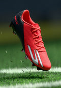 Roter und schwarzer Fußballschuh mit silbernen Akzenten, der Gras auf einem markierten grünen Feld aufwirbelt.