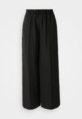 Schwarze weit geschnittene Hose aus strukturiertem Stoff. Sie verfügen über einen dehnbaren Bund mit Kordelzug und vertikalen Falten für zusätzliche Details.