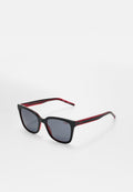 Schwarze rechteckige Sonnenbrille mit dunklen Gläsern und roten Akzenten im inneren Rahmen, mit dem Markennamen „HUGO“ auf Bügeln und Gläsern, vor weißem Hintergrund.
