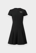 Schwarzes Kleid mit kurzen Ärmeln, eng anliegendem Oberteil, ausgestelltem Rock, Reißverschluss hinten und einem silbernen Schleifenakzent auf der linken Seite. Glatte Stoffoberfläche.