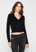 Schwarzer, kurz geschnittener Strickpullover mit tiefem V-Ausschnitt und langen Ärmeln. Mit gerippten Details am Saum. Kombiniert mit schwarzen, eng anliegenden Jeans.