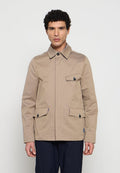 Mann trägt beige Jacke mit Knöpfen und drei Klappentaschen sowie schwarze Hose, steht vor schlichtem hellem Hintergrund und schaut nach vorne.