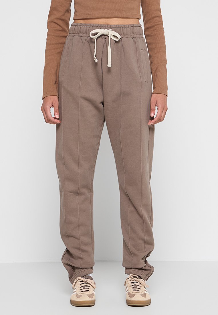 Braune Sweatpants mit schmal zulaufendem Design, elastischem Bund und Kordelzug. Verfügt über Seitentaschen und sichtbare Steppnähte für Textur.