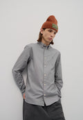 Graues Button-Down-Hemd mit Kragen, leichtes Material und dezentem Logo. Kombiniert mit einer gestrickten orangen Beanie mit Logo-Patch.