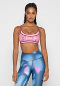 Frau mit geflochtenem Haar, die einen rosa gemusterten Sport-BH und eine hochtaillierte blaue Leggings mit pinken und lila abstrakten Designs trägt.