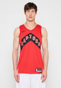 Mann trägt ein rotes Toronto Raptors Basketballtrikot mit schwarzer und weißer Schrift, steht vor einem schlichten hellen Hintergrund.