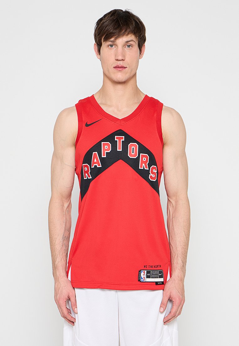 Mann trägt ein rotes Toronto Raptors Basketballtrikot mit schwarzer und weißer Schrift, steht vor einem schlichten hellen Hintergrund.