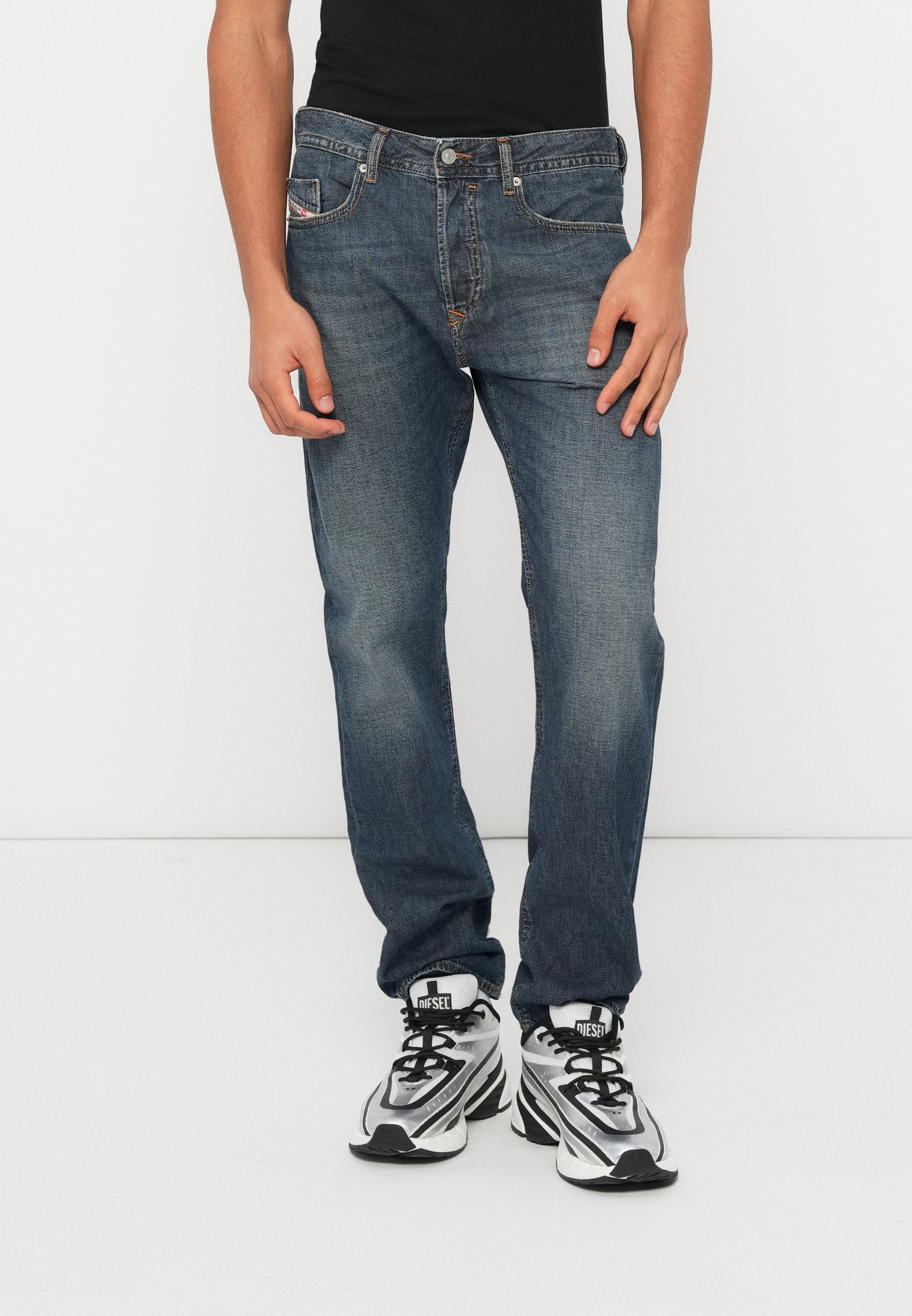 Blaue Denim-Jeans mit geradem Schnitt, Vordertaschen und Reißverschluss. Dazu schwarze Sneaker mit silbernen Details und schwarzen Schnürsenkeln.