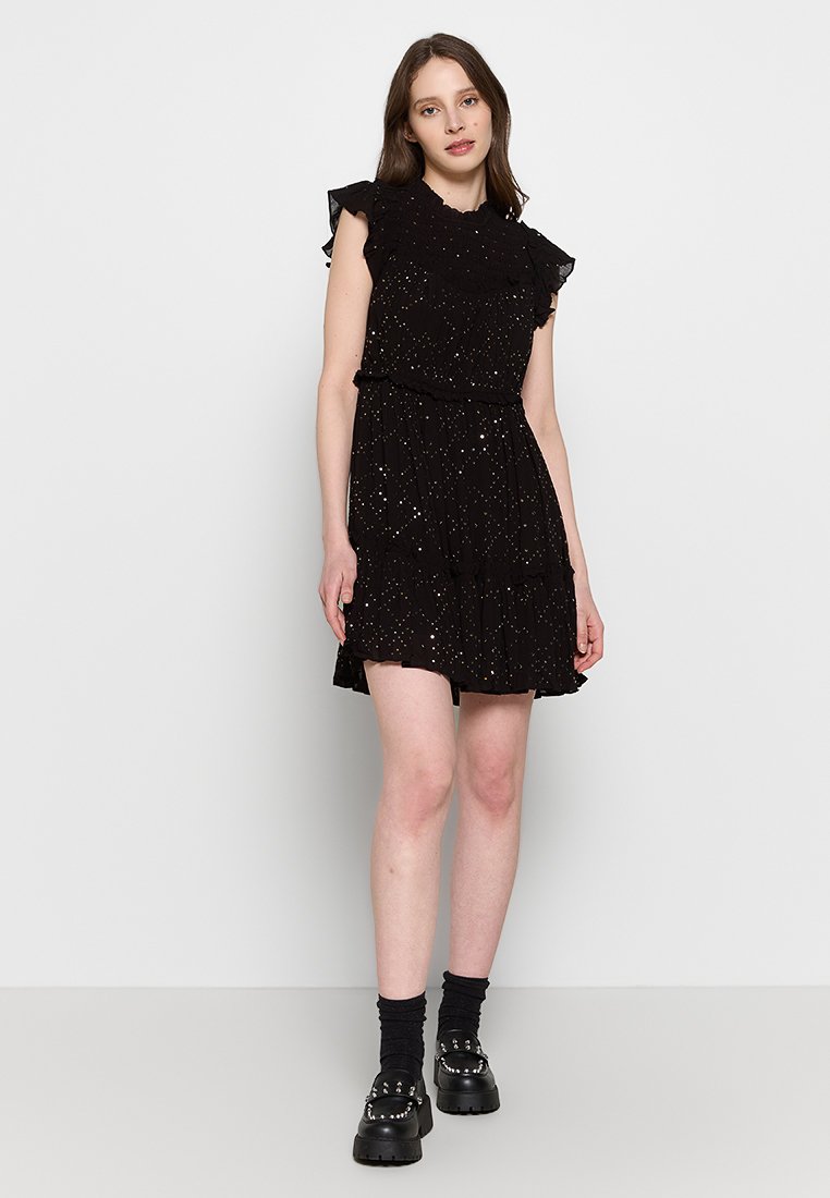 Schwarzes Kleid mit Rüschensleevs, gestuftem Rock und verstreuten metallischen Akzenten. Getragen mit schwarzen Plateau-Schuhen und knielangen Socken.