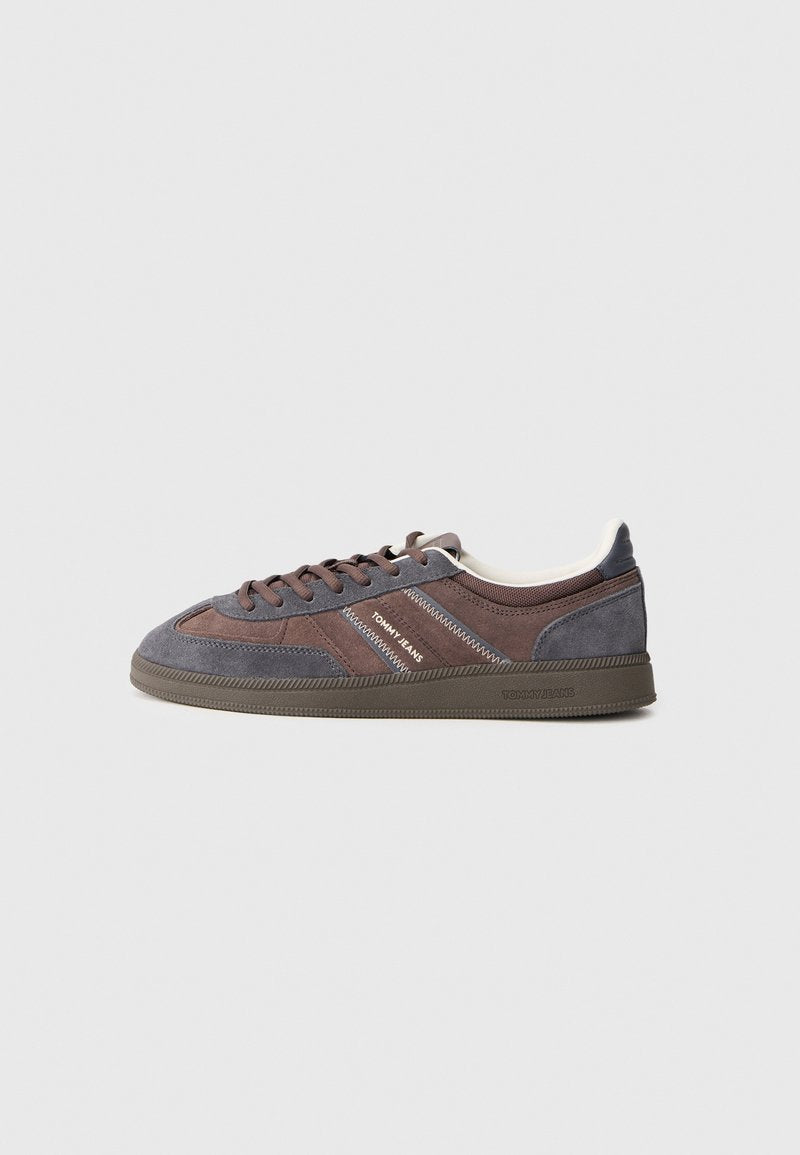 Low-Top-Sneaker aus braunem und grauem Wildleder mit "Tommy Jeans"-Branding an der Seite und an der Sohle, vor einem hellgrauen Hintergrund.