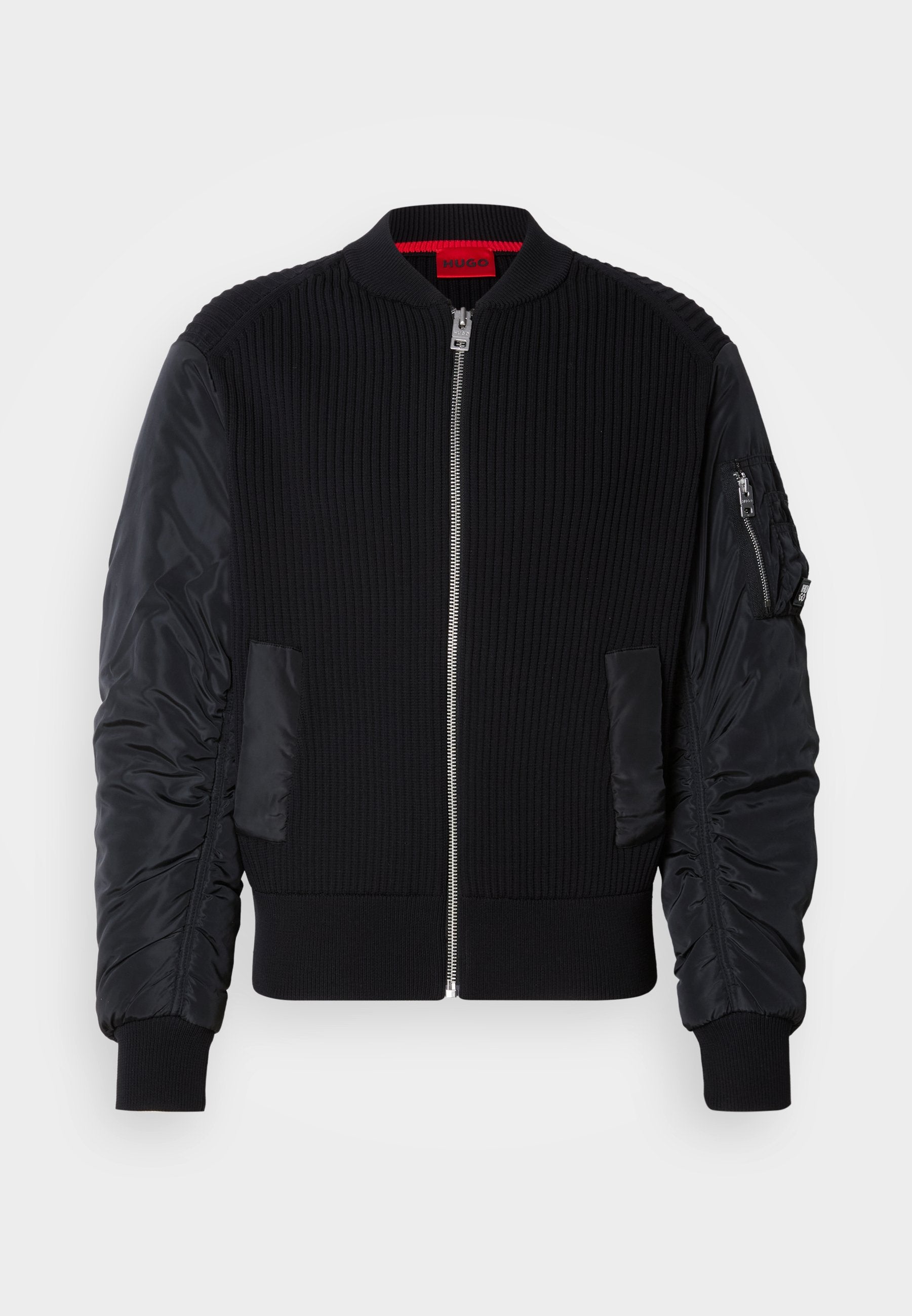 Schwarze Bomberjacke mit geripptem Strickkörper und glatten Nylonärmeln, Reißverschluss vorne und Seitentaschen. Figurbetonter Schnitt mit umgeschlagenen Saumen.