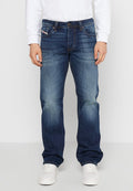 Dunkelblaue Jeans aus Denim mit geradem Bein Schnitt, die leichte Verblassungen aufweisen, mit einem Knopfverschluss und fünf Taschen, getragen mit weißen Turnschuhen.
