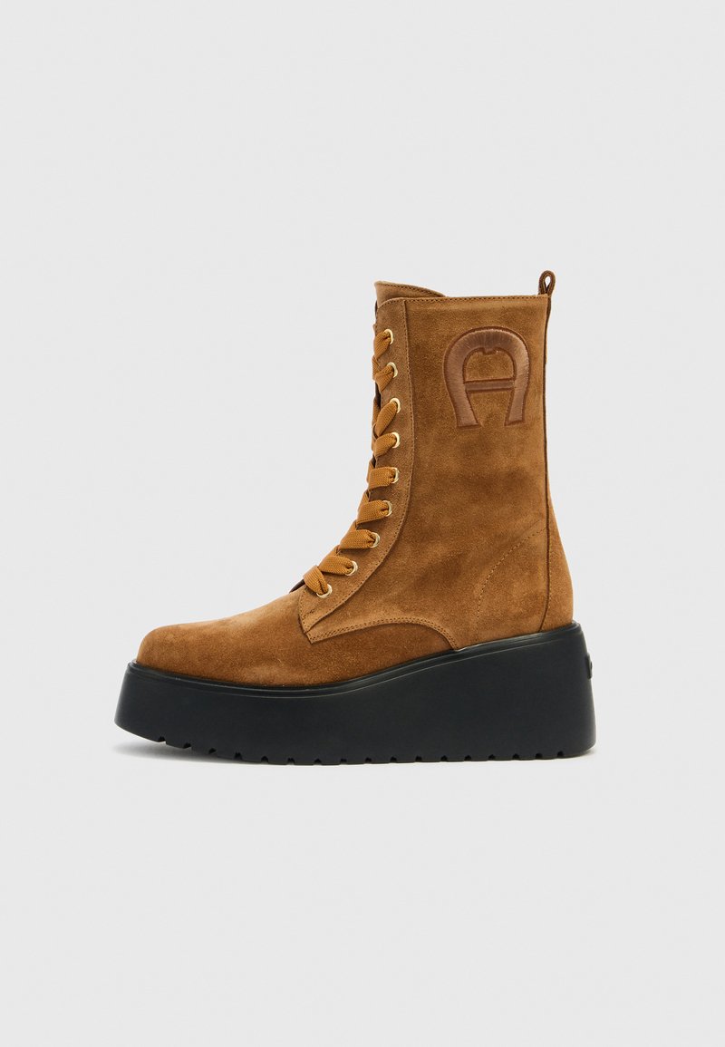 Brauner Wildleder-Stiefelette mit goldenen Ösen, Schnürung vorne, erhöhter Plateau-Sohle und geprägt-logo Detail an der Seite.