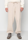 Mann in beigen Sweatpants mit Kordelzugbund und elastischen Bündchen, kombiniert mit grau-braunen Sneakers, steht vor einem schlichten Hintergrund.