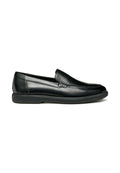 Schwarze Leder-Slipper mit Stitzdetail, niedrigem Absatz und Gummisohle, seitlich auf einem weißen Hintergrund dargestellt.