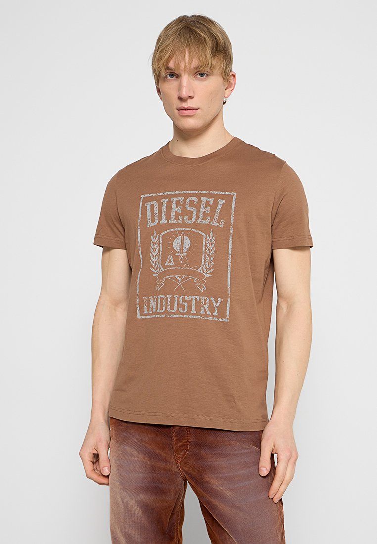 Braunes Baumwoll-T-Shirt mit Rundhalsausschnitt und kurzen Ärmeln, das einen verblassten grauen Grafikdruck zeigt, auf dem in einem Kästchen-Design "DIESEL INDUSTRY" steht.