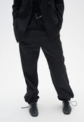 Schwarze, locker sitzende Hosen mit einem elastischen Bund und Kordelzug. Glatte Textur mit leicht glänzendem Finish, kombiniert mit schwarzen Geschäftsschuhen.