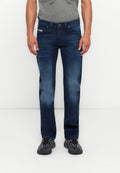 Mann in dunkelblauen lässigen Jeans, grauem T-Shirt und schwarzen Turnschuhen, der vor einem schlichten weißen Hintergrund steht.