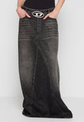 Schwarzer, ausgebleichter Denim-Maxikleid mit einer asymmetrischen Naht und einer ovalen silbernen Gürtelschnalle, getragen mit Händen in den Taschen und einem schwarzen Oberteil.