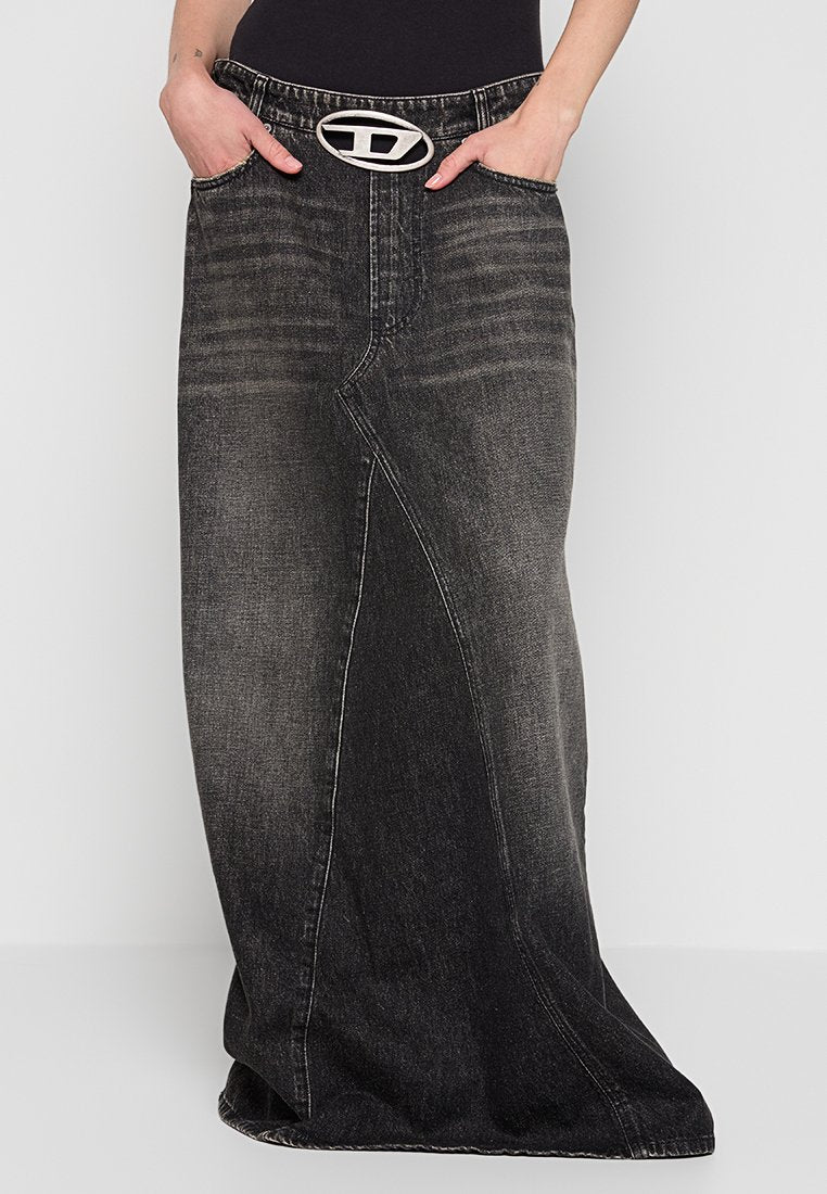 Schwarzer, ausgebleichter Denim-Maxikleid mit einer asymmetrischen Naht und einer ovalen silbernen Gürtelschnalle, getragen mit Händen in den Taschen und einem schwarzen Oberteil.