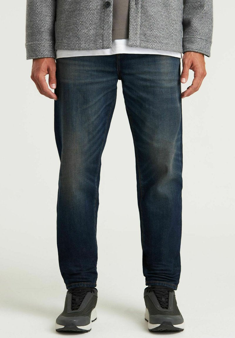 Dunkelblaue Denim-Jeans mit geradem Beinschnitt, die eine subtile Ausbleichung, kontrastierende Nähte und eine abgenutzte Textur aufweisen. Kombiniert mit schwarzen Sneakers.