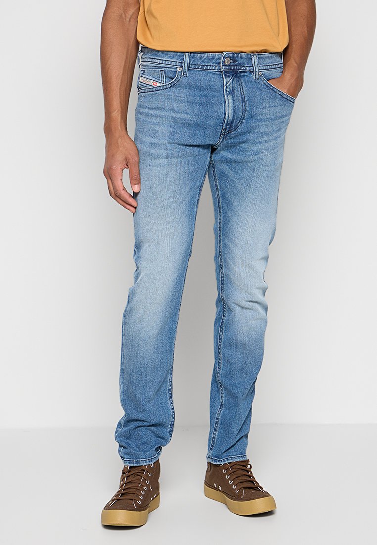 Hellblaue Jeans aus Denim mit geradem Schnitt, ausgewaschenem Finish, fünf Taschen und dezenten Stickdetails. Kombiniert mit braunen High-Top-Sneakern.