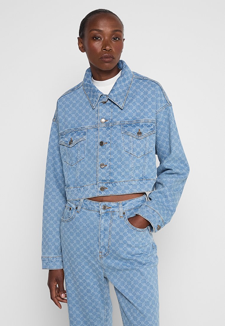 Gekürzte Jeansjacke in Hellblau mit gemustertem Textur, zwei Brusttaschen, Knopfverschluss und kontrastierenden Nähten.