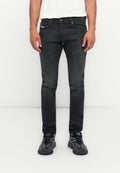 Mann in eng geschnittenen, ausgebleichten schwarzen Jeans mit dezenten Used-Effekten und schwarzen Diesel-Sneakern, vor einem schlichten weißen Hintergrund stehend.