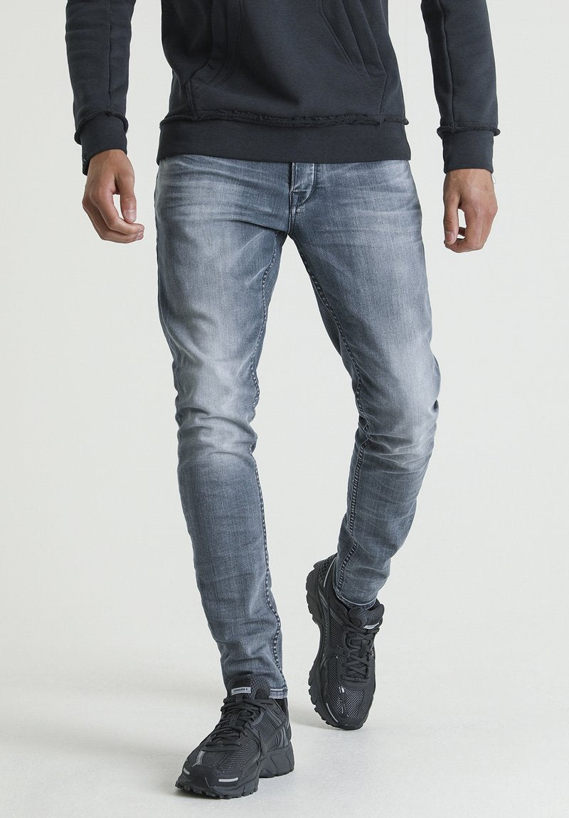Schmal geschnittene, verblasste blaue Jeans mit einer smoothen Textur, die ein klassisches Fünf-Taschen-Design aufweisen. Getragen mit schwarzen Sportschuhen.