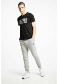 Schwarzes Baumwoll-T-Shirt mit "ALPHA INDUSTRIES" in Weiß bedruckt, kombiniert mit grauen Jogginghosen und weißen Sportschuhen mit schwarzen Akzenten.
