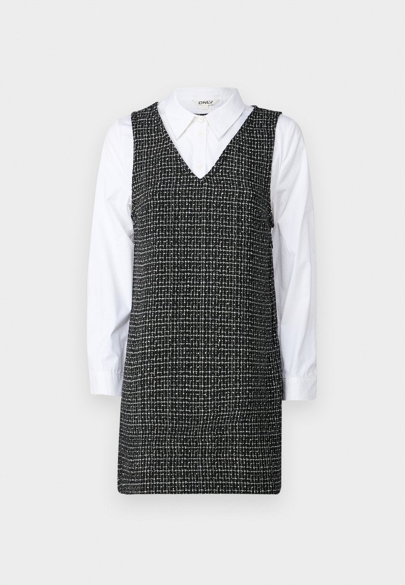 Schwarz-weiß kariertes Kleid mit V-Ausschnitt und ärmellosem Design, über einem weißen, langärmligen Hemd mit Kragen geschichtet.