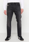 Dunkelgraue Jeans aus Denim mit geradem Schnitt, Fünf-Taschen-Design, subtilen Verfärbungen und metallischen Details. Getragen mit schwarzen Sneakers.