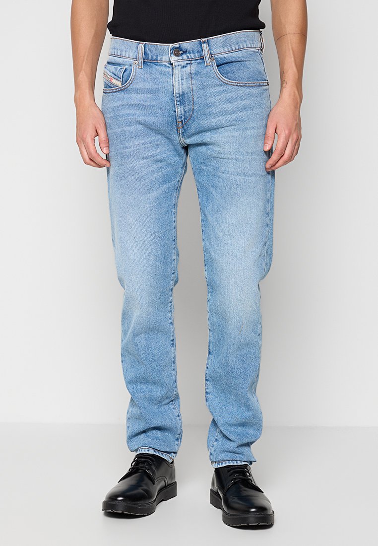 Hellblaue Denim-Jeans mit geradem Schnitt, ausgestattet mit einem klassischen Fünf-Taschen-Design und subtilem Verblassen, kombiniert mit schwarzen Dressschuhen.