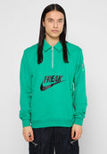 Junge Person mit langen schwarzen Haaren, die einen grünen Zip-Up-T sweatshirt mit "FREAK" und dem Nike-Logo sowie schwarze Hosen mit Reißverschluss-Taschen trägt.