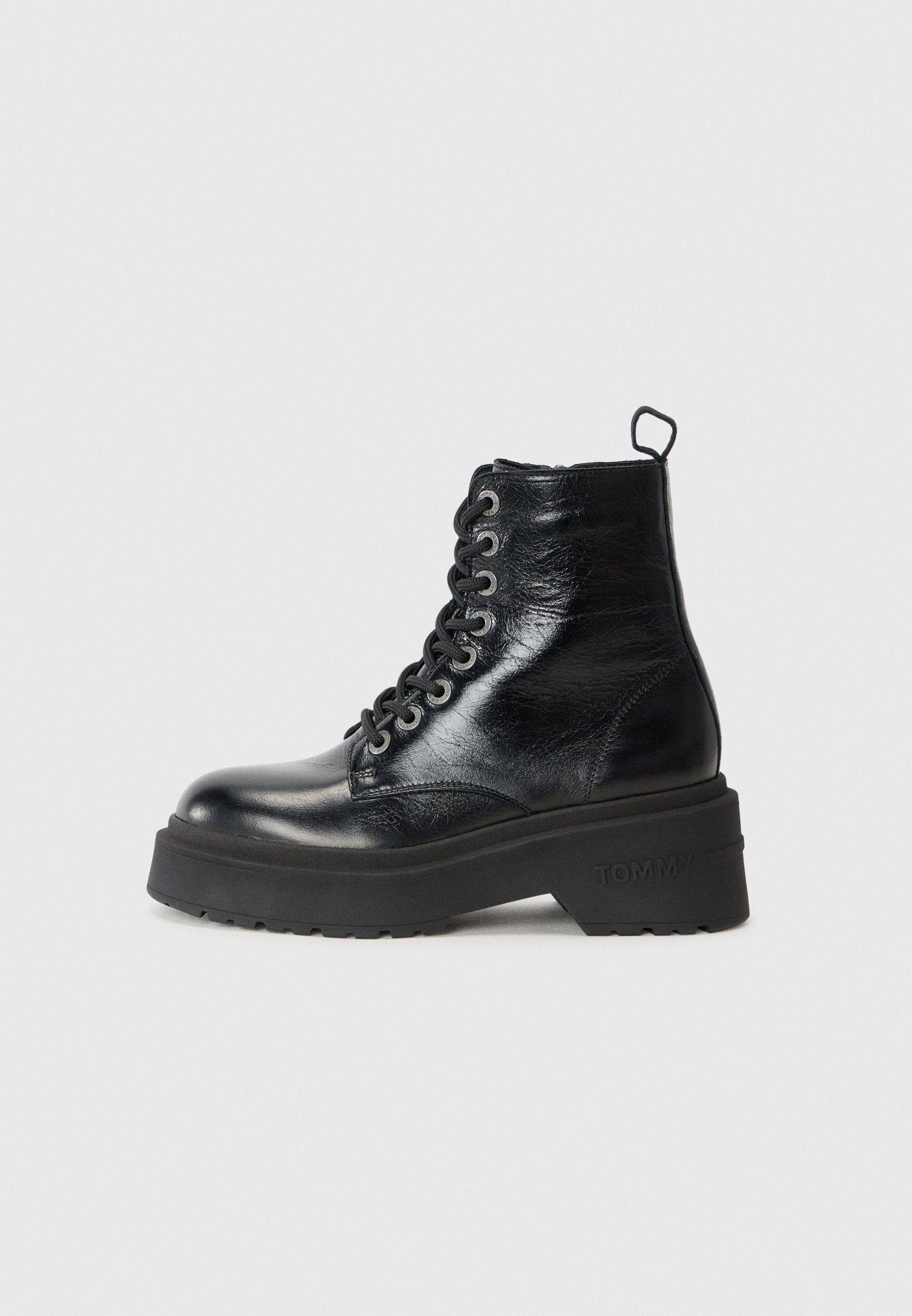Schwarze Stiefeletten mit glänzender Oberfläche, ausgestattet mit einer klobigen Plattformsohle und Schnürdesign, auf denen die Marke "TOMMY" deutlich zu sehen ist.