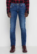Mann trägt mittelblaue Slim-Fit-Jeans, rot-schwarz karierte Hemd und dunkelrote glänzende Turnschuhe, steht vor einem einfarbigen Hintergrund.