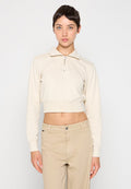 Beige Sweatshirt mit kurzem Schnitt, Reißverschlusskragen und kleinem Logo auf der Brust. Langärmlig mit geripptem Saum. Kombiniert mit hellbeigen Hosen.