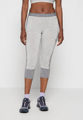 Frau trägt hellgraue, gekürzte Leggings mit dunkelgrauen Bündchen, passenden Sport-BH, lila Socken und schwarz-pinke Sneakers, stehend.