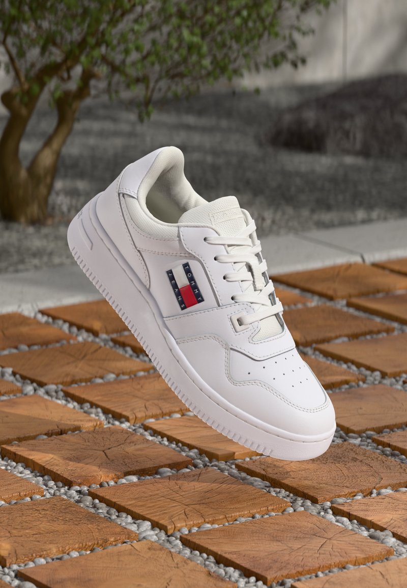 Weiße Ledersneaker mit glatter Textur, Schnürdesign, durchlöchtem Zehenbereich und roten, weißen und blauen Streifenakzenten an der Seite.